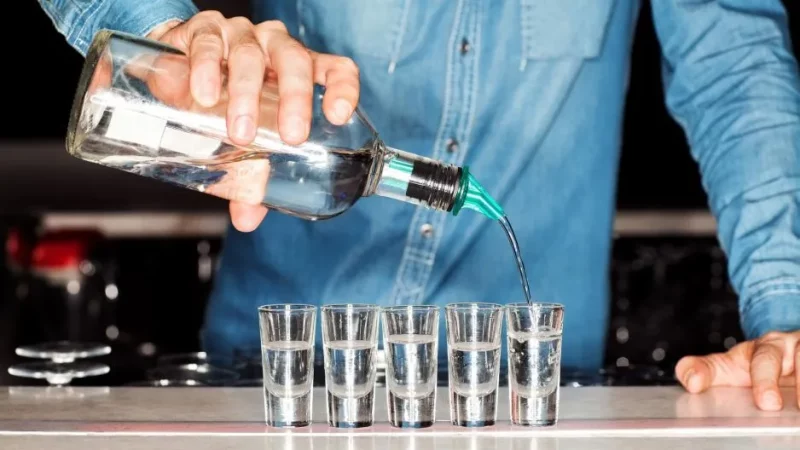 Бармен разливает водку в шоты