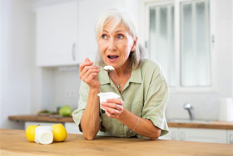 Пожилая женщина ест йогурт