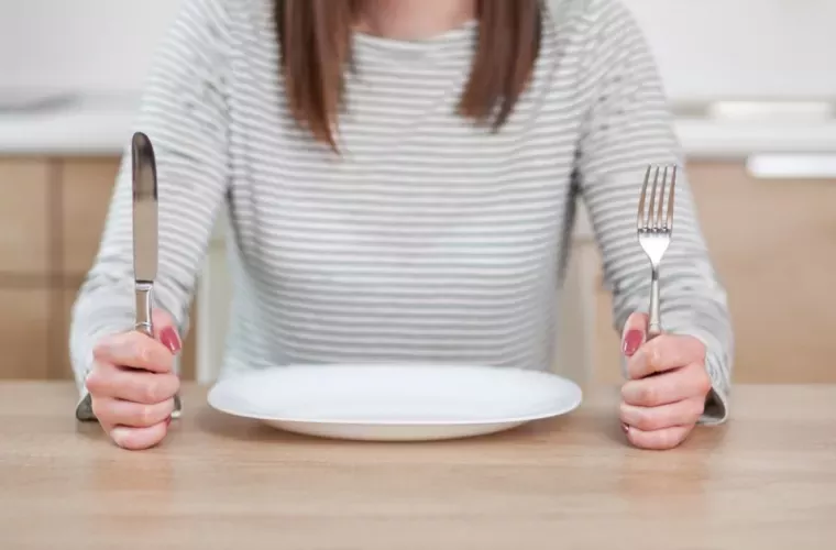 Девушка сидит с пустой тарелкой и приборами